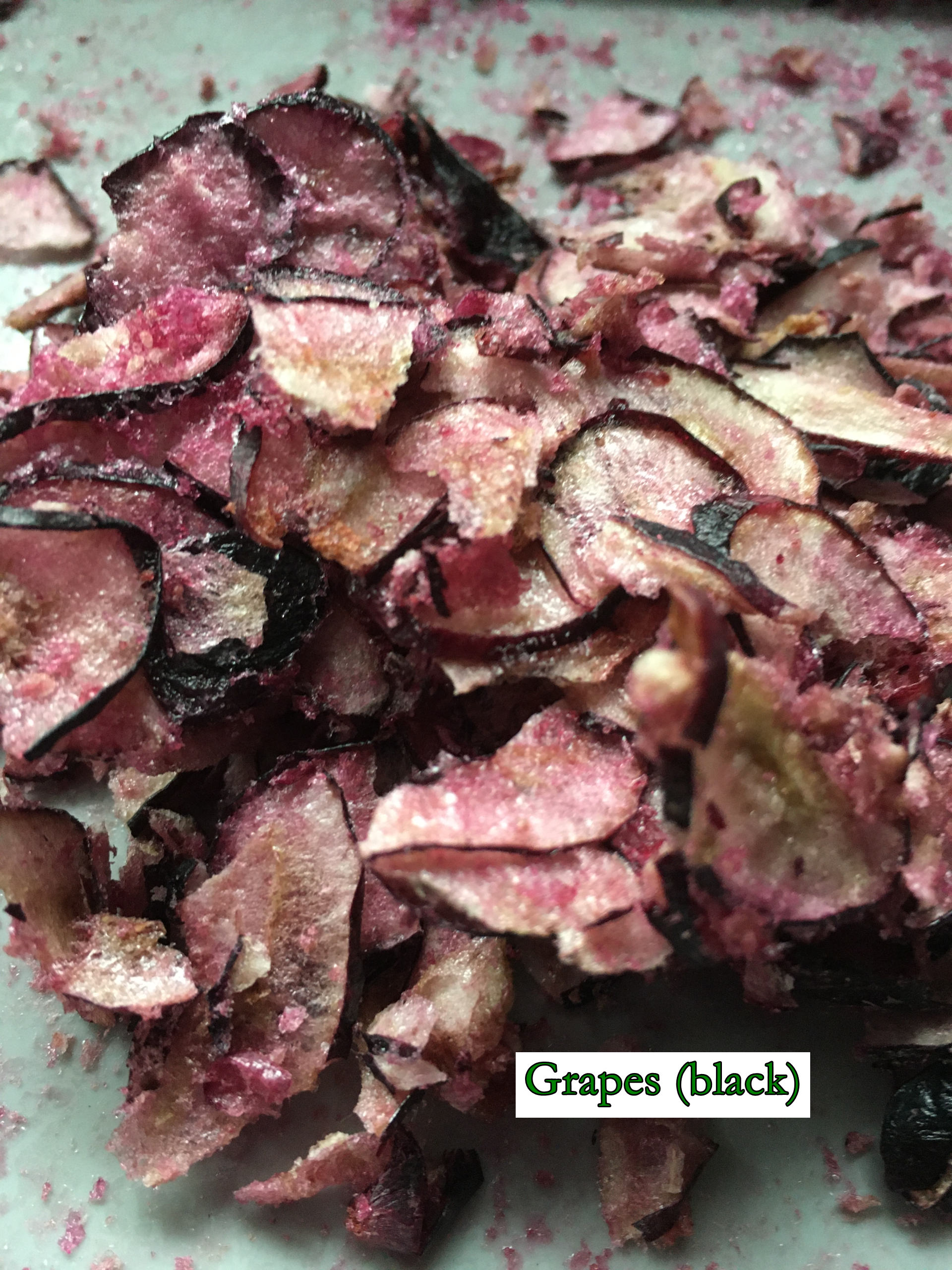 freeze-dried black grapes, thinly sliced, some of the sugar caramelised on drying, visible dark red skins and light red crystals of sweet grape juice that have dried up