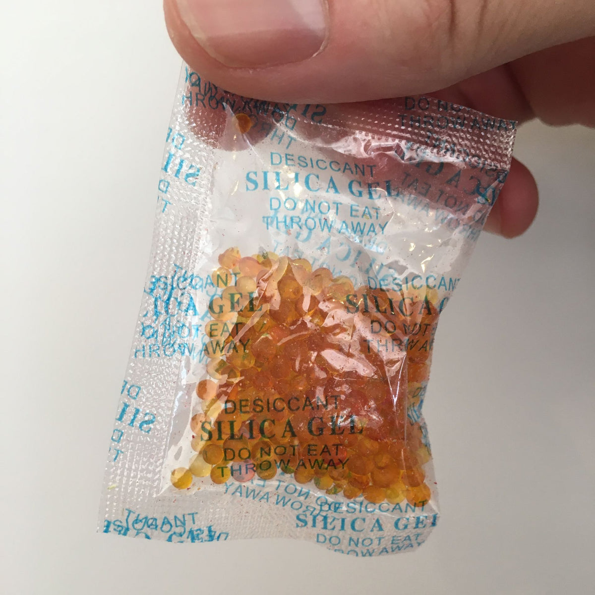 Silica gel packet held by a hand with a white background
