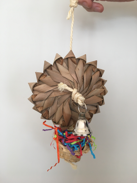flower made from palm leaf on top of a wicker basket stuffed with shredded paper. the back has a metal bell.