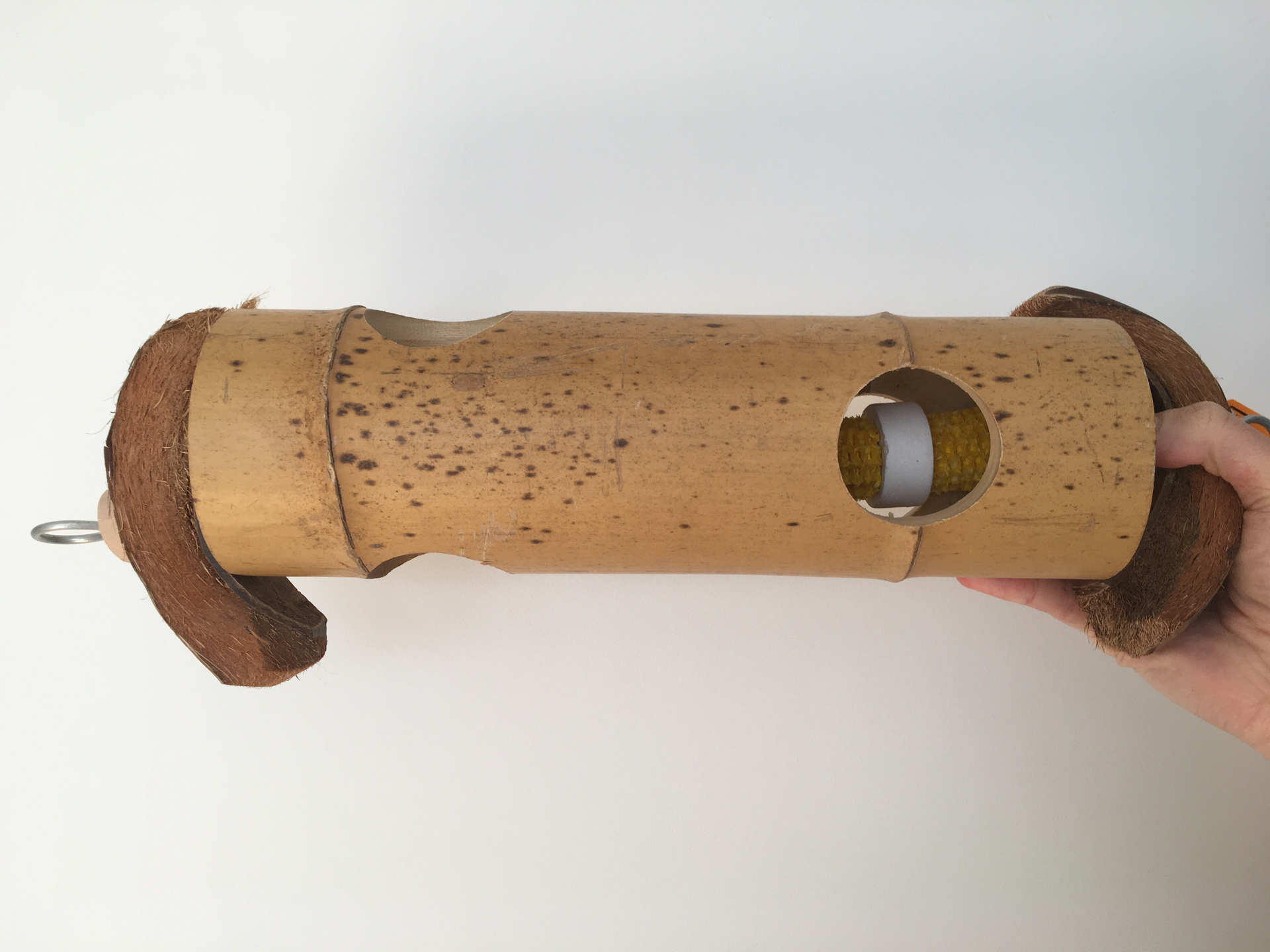 This is a big log toy with holes where you can hide treats. Some corn husks and calcium blocks are already placed inside, and the log is capped off with coconut husks. You could hang the toy horizontally