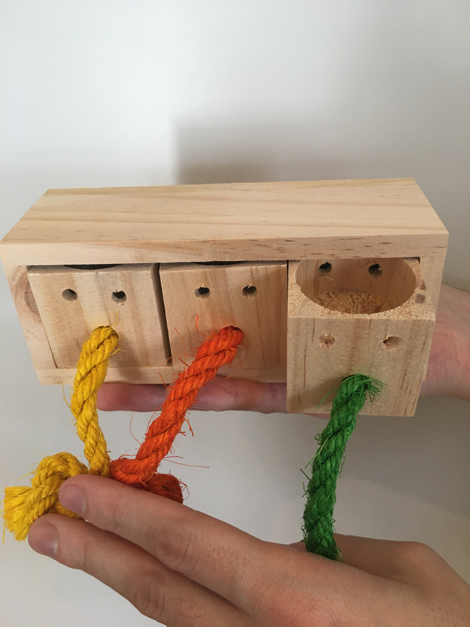 a wooden block with cops and colourful ropes to pull on. One cup is pulled out.